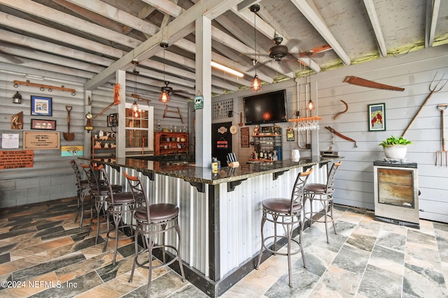 bar featuring beamed ceiling, ceiling fan, dark stone counters, and hanging light fixtures