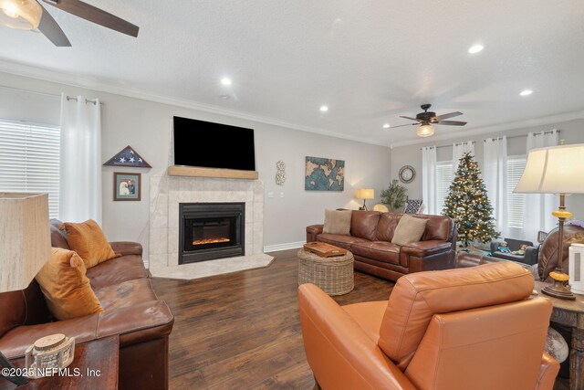 living room with dark hardwood / wood-style floors, ceiling fan, ornamental molding, and a tiled fireplace