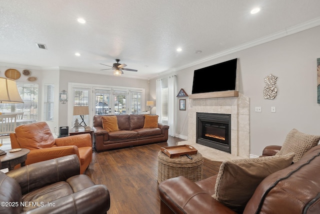 living room with dark wood-type flooring, ceiling fan, ornamental molding, a textured ceiling, and a fireplace