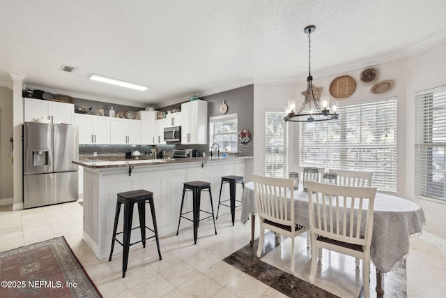 kitchen featuring stainless steel appliances, kitchen peninsula, a chandelier, a textured ceiling, and white cabinets