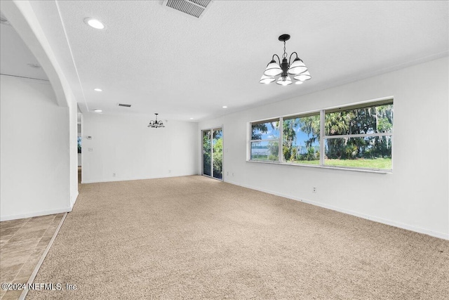 empty room featuring a notable chandelier, a textured ceiling, and light colored carpet