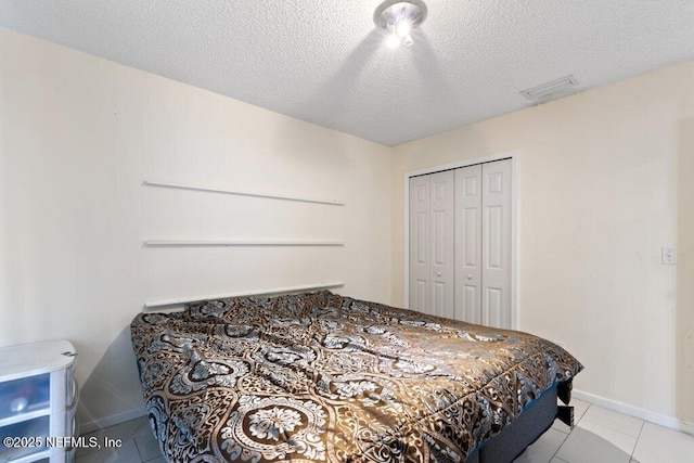 bedroom with light tile patterned floors, baseboards, visible vents, a textured ceiling, and a closet