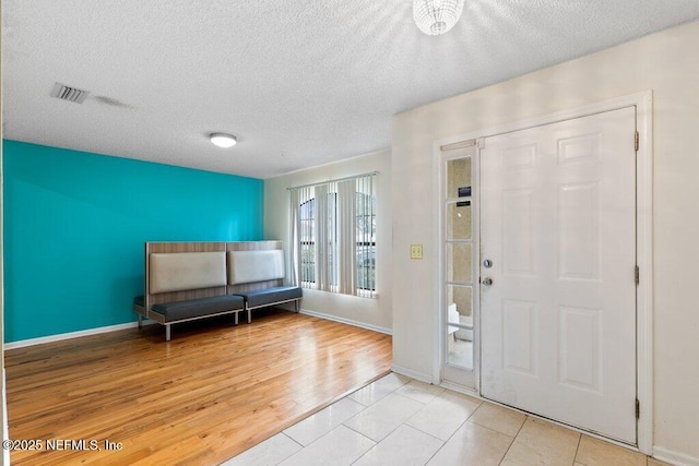 foyer featuring light wood-type flooring, baseboards, visible vents, and a textured ceiling