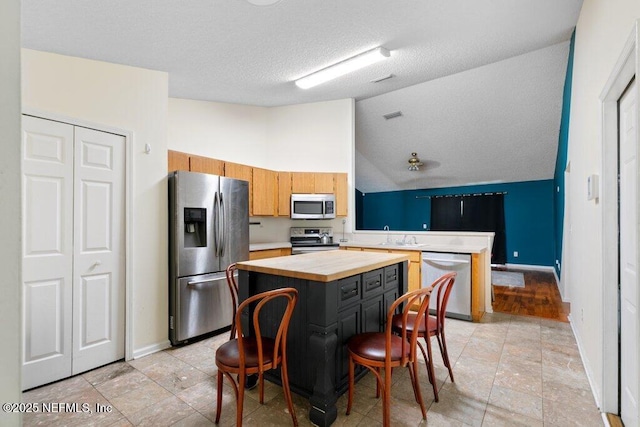 kitchen with a center island, lofted ceiling, appliances with stainless steel finishes, a sink, and baseboards