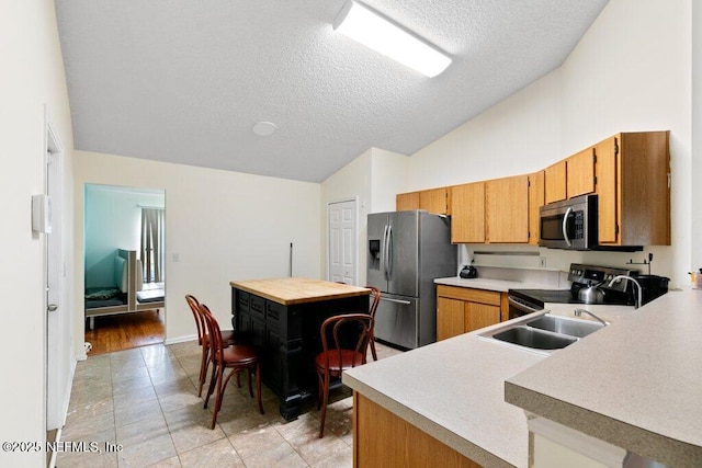 kitchen with brown cabinetry, a textured ceiling, stainless steel appliances, and light countertops