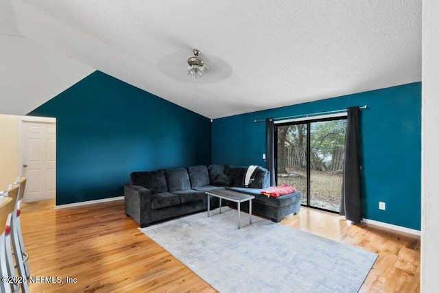 living area featuring vaulted ceiling, a textured ceiling, baseboards, and wood finished floors