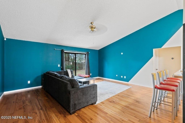 living room with a ceiling fan, a textured ceiling, baseboards, and wood finished floors