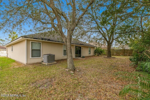 rear view of house featuring fence, central AC unit, and a lawn