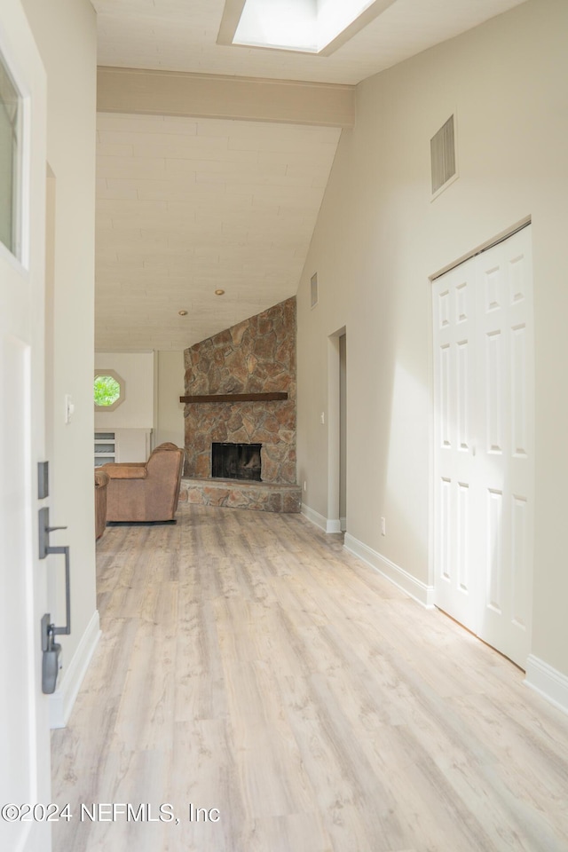 unfurnished living room with a skylight, a stone fireplace, wood finished floors, high vaulted ceiling, and baseboards