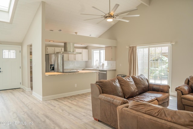 living area with high vaulted ceiling, a skylight, baseboards, and light wood finished floors