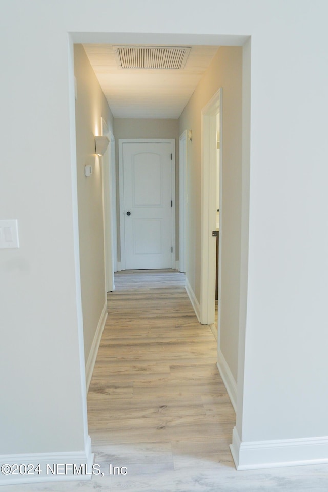 hall featuring light wood finished floors, baseboards, and visible vents