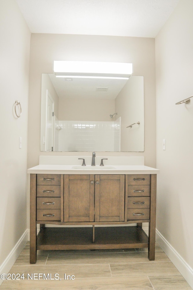 full bathroom featuring wood tiled floor, baseboards, walk in shower, and vanity