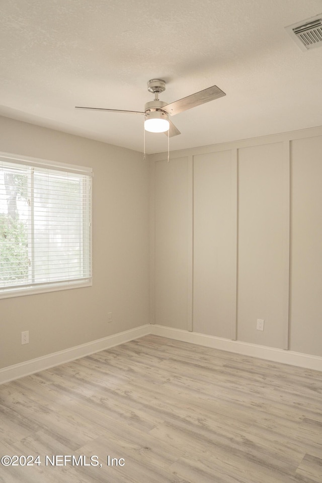 spare room featuring ceiling fan, a textured ceiling, visible vents, baseboards, and light wood-type flooring