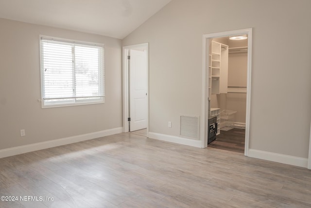 unfurnished bedroom with a walk in closet, lofted ceiling, visible vents, light wood-style flooring, and baseboards