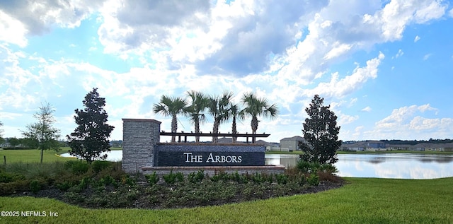 community / neighborhood sign featuring a water view and a lawn