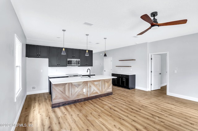 kitchen with ceiling fan, plenty of natural light, a kitchen island with sink, and light wood-type flooring