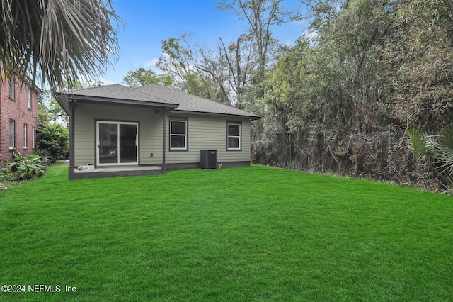 rear view of house with central air condition unit and a lawn