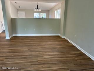 unfurnished dining area featuring dark wood-style floors, a notable chandelier, and baseboards