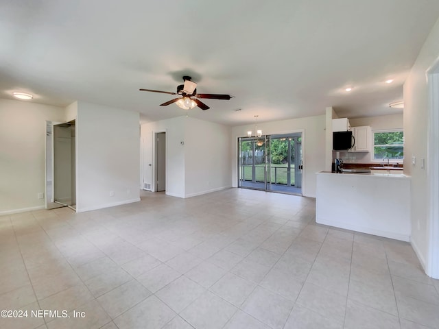 unfurnished living room featuring ceiling fan with notable chandelier, light tile patterned floors, and sink