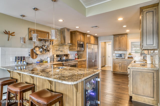 kitchen with built in appliances, wall chimney exhaust hood, tasteful backsplash, hanging light fixtures, and hardwood / wood-style flooring