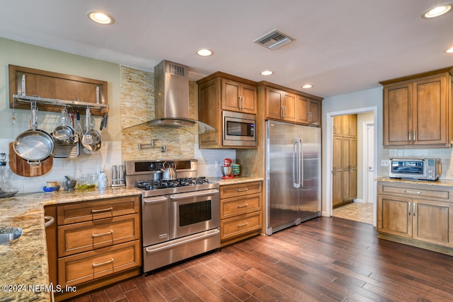 kitchen with built in appliances, tasteful backsplash, wall chimney exhaust hood, and dark hardwood / wood-style flooring