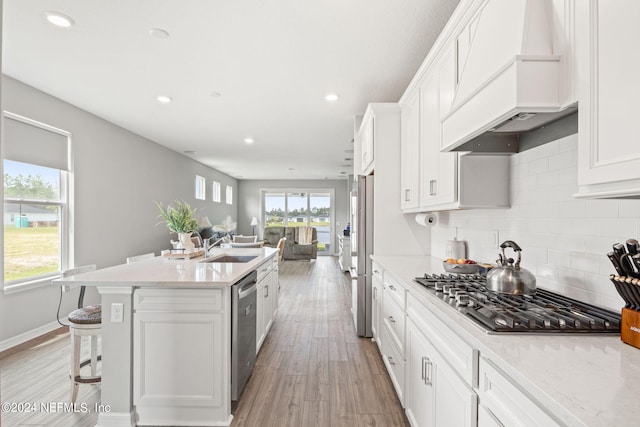 kitchen with light wood-type flooring, white cabinets, appliances with stainless steel finishes, and custom range hood