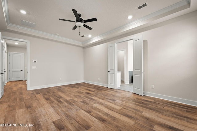 empty room featuring baseboards, visible vents, wood finished floors, a tray ceiling, and crown molding