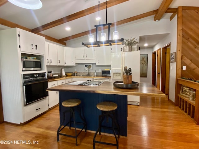 kitchen with light hardwood / wood-style flooring, lofted ceiling with beams, white cabinetry, stainless steel appliances, and pendant lighting