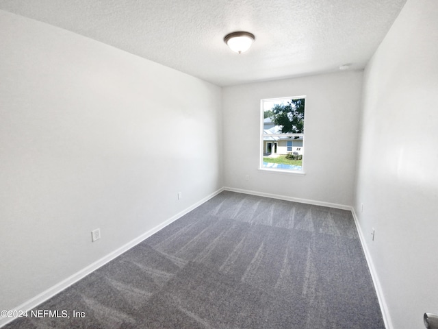 empty room with dark carpet, a textured ceiling, and baseboards