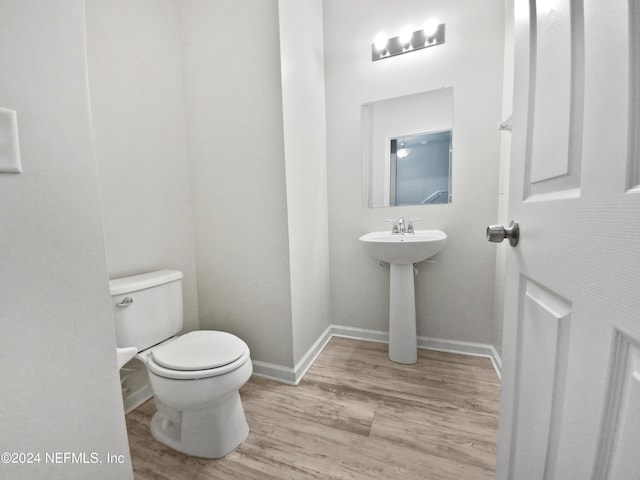 half bathroom with wood finished floors, toilet, and baseboards