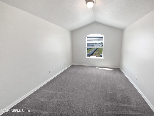 spare room with vaulted ceiling, dark carpet, a textured ceiling, and baseboards