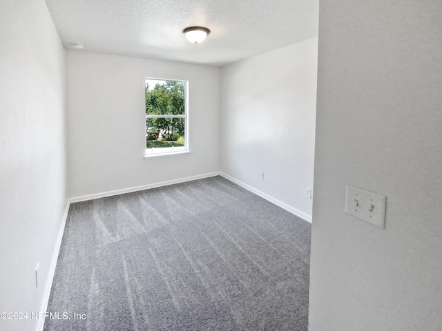 spare room with a textured ceiling, carpet floors, and baseboards