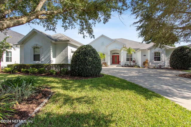 ranch-style house featuring a front lawn, concrete driveway, and stucco siding