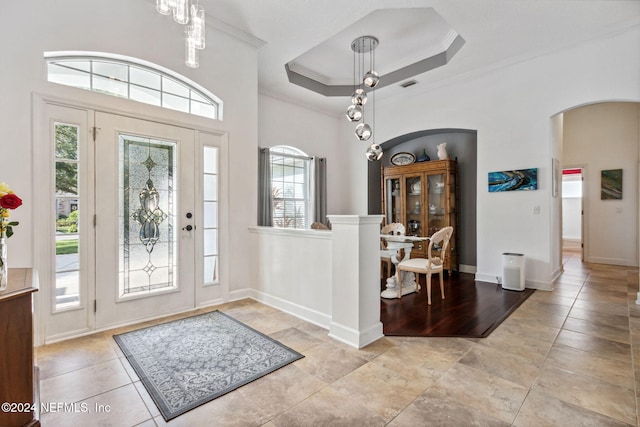 foyer with arched walkways, visible vents, baseboards, ornamental molding, and a raised ceiling