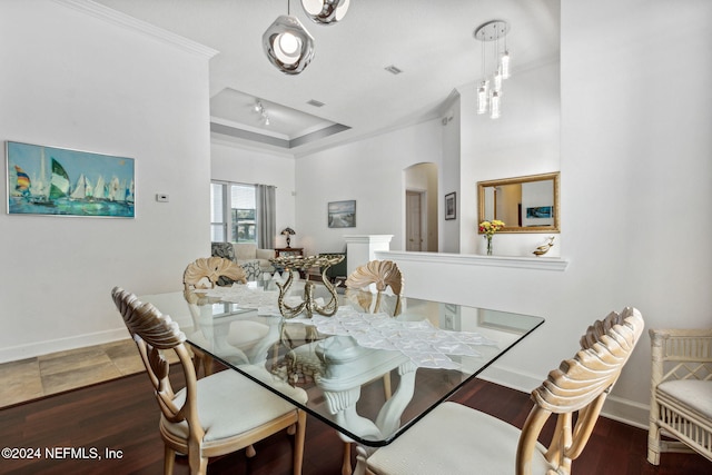 dining area with arched walkways, dark wood-style flooring, baseboards, a raised ceiling, and crown molding