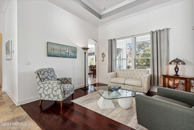 living area with arched walkways, wood finished floors, baseboards, a tray ceiling, and crown molding