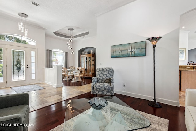 living room featuring a tray ceiling, visible vents, arched walkways, and wood finished floors