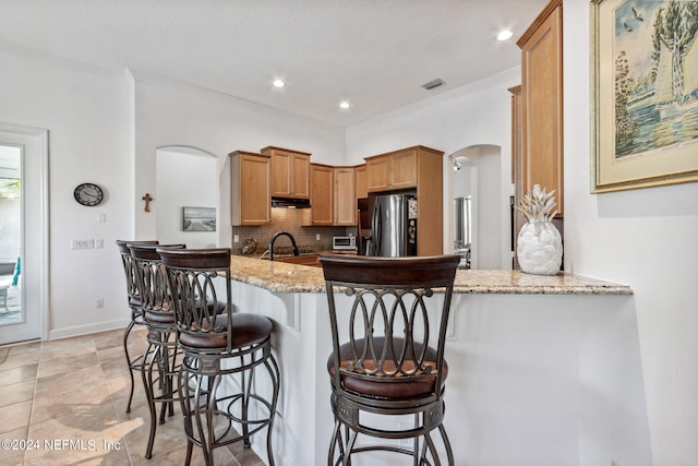 kitchen featuring a peninsula, light stone countertops, stainless steel fridge, and arched walkways