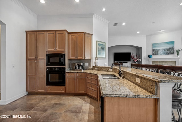 kitchen featuring a sink, black appliances, light stone countertops, a peninsula, and a kitchen bar