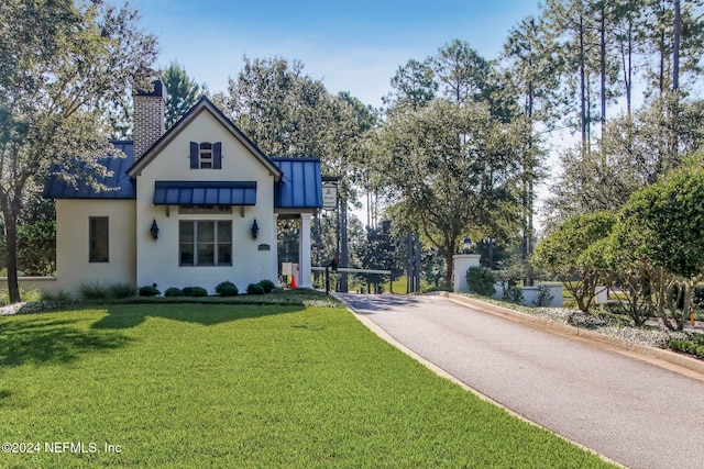 modern farmhouse style home featuring metal roof, driveway, stucco siding, a chimney, and a front yard