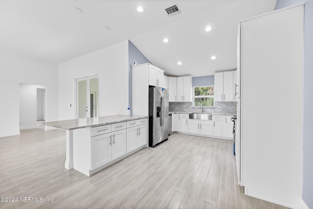 kitchen featuring decorative backsplash, stainless steel refrigerator with ice dispenser, white cabinets, light stone counters, and sink