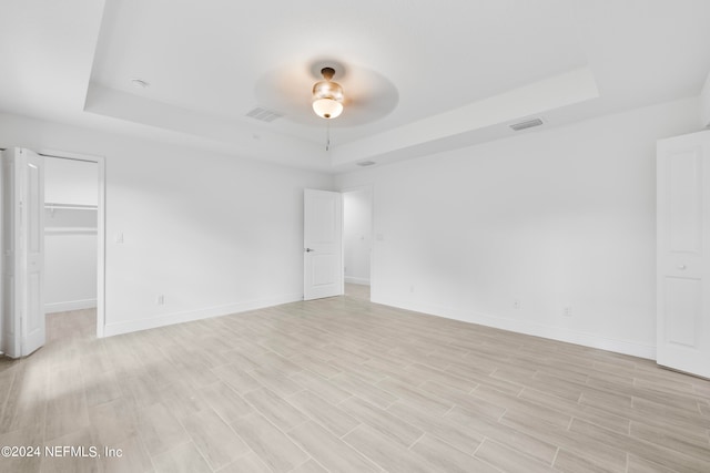 spare room with ceiling fan, light hardwood / wood-style floors, and a tray ceiling