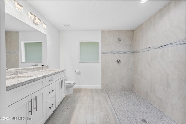 bathroom with double vanity, tiled shower, and toilet