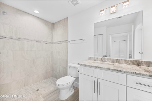 bathroom with toilet, a tile shower, and vanity