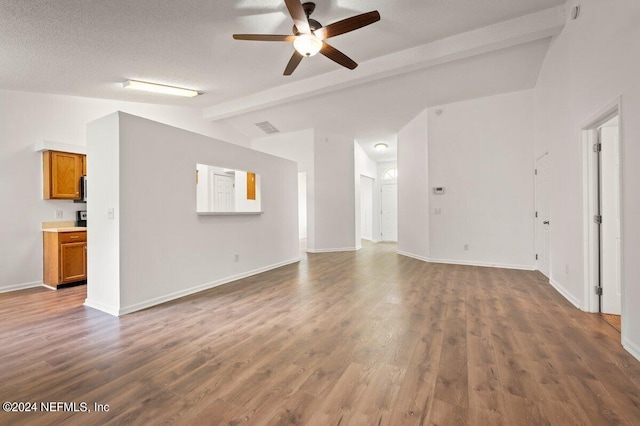 unfurnished living room featuring ceiling fan, hardwood / wood-style flooring, lofted ceiling with beams, and a textured ceiling