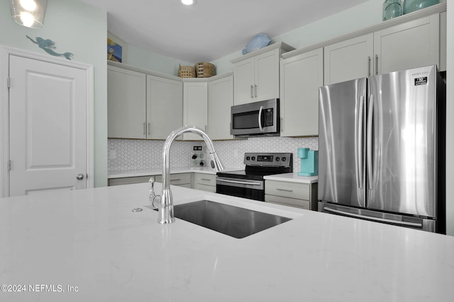 kitchen with sink, stainless steel appliances, tasteful backsplash, and light stone countertops