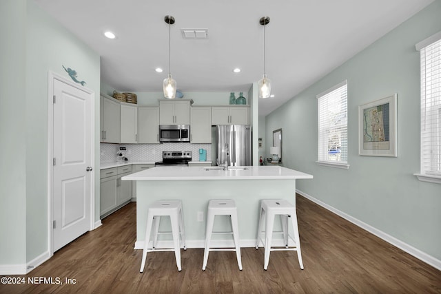 kitchen featuring decorative backsplash, dark hardwood / wood-style floors, appliances with stainless steel finishes, decorative light fixtures, and a center island with sink