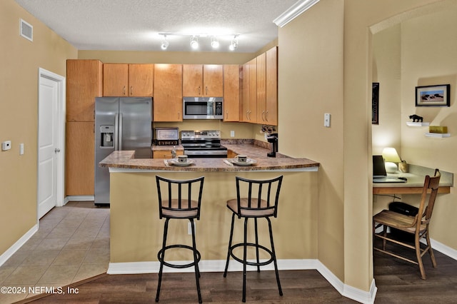 kitchen featuring a textured ceiling, a breakfast bar area, stainless steel appliances, a peninsula, and visible vents