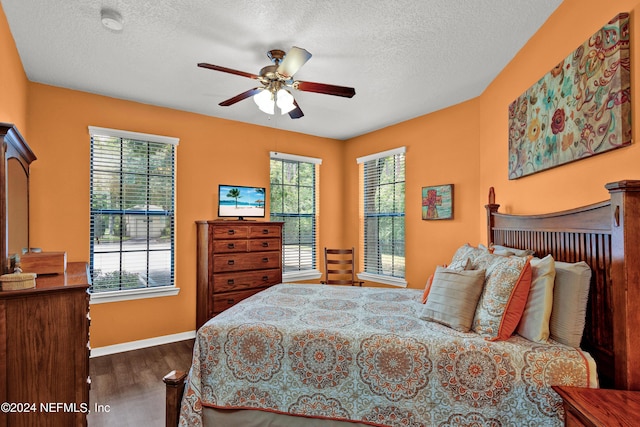 bedroom with a textured ceiling, multiple windows, baseboards, and dark wood-style flooring