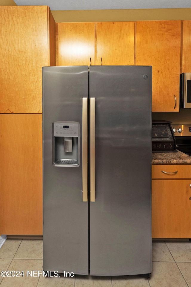 kitchen with light tile patterned floors, stainless steel appliances, and dark stone counters